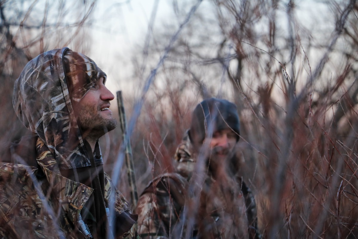 Person wearing a camo hat outdoors in a wooded setting
