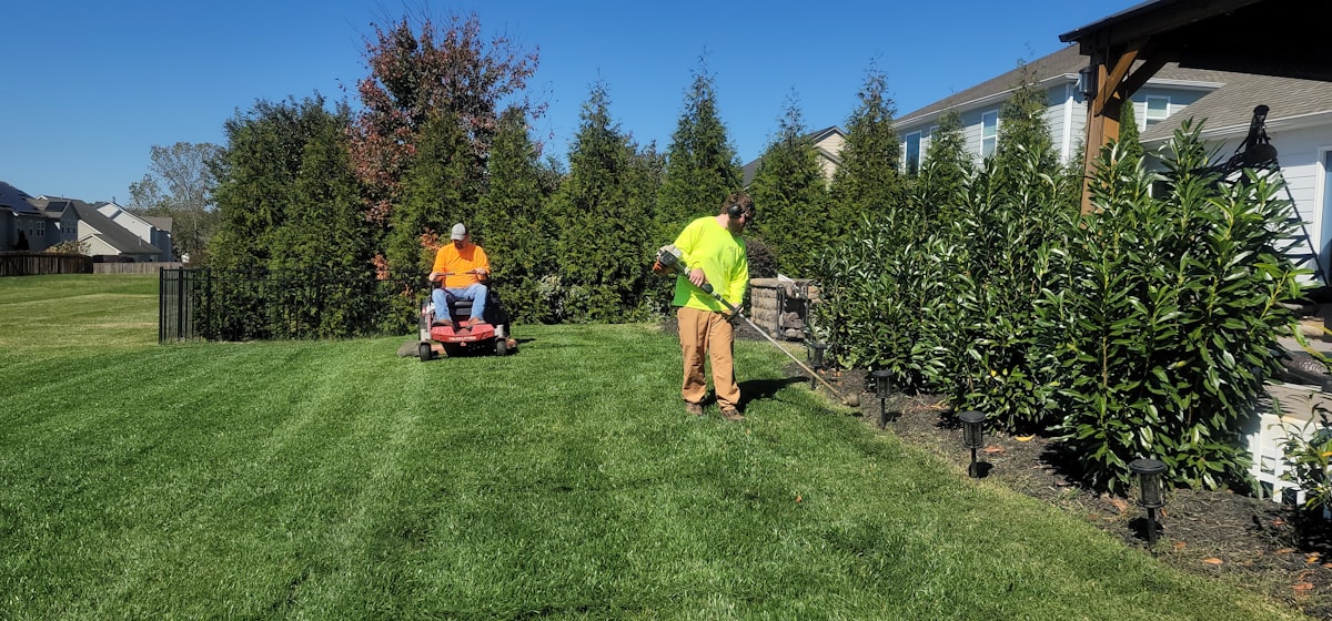 Lawn care crew member mowing a lawn in a branded hat